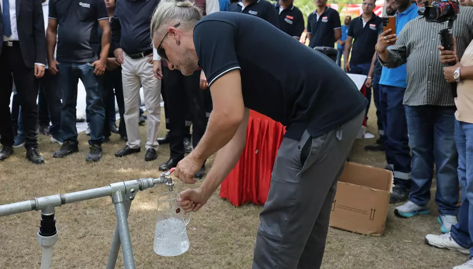 Un expert Veoliaforce servant de l'eau potable traitée depuis le robinet d'une unité mobile dans une carafe devant la délégation.