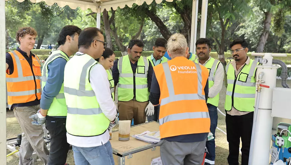 Group of employees in safety vests listening to a trainer during a hands-on workshop around water purification equipment.