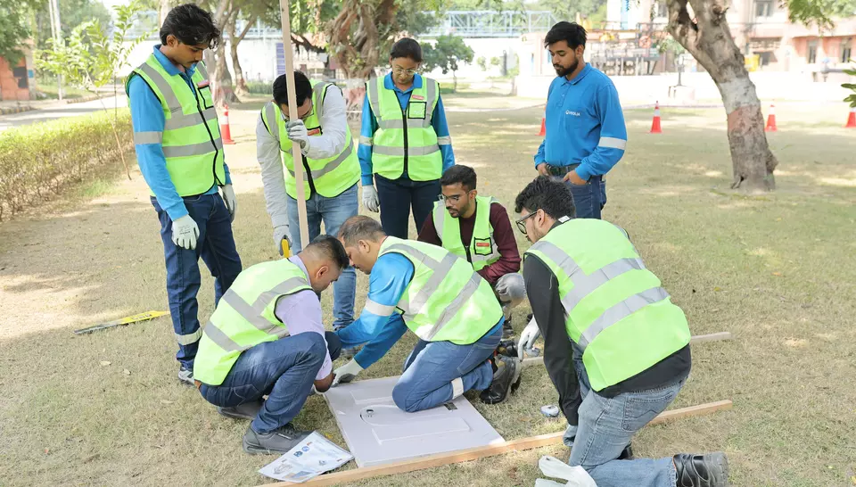 Employees kneeling on the grass assembling a technical module on the ground during a practical training exercise.